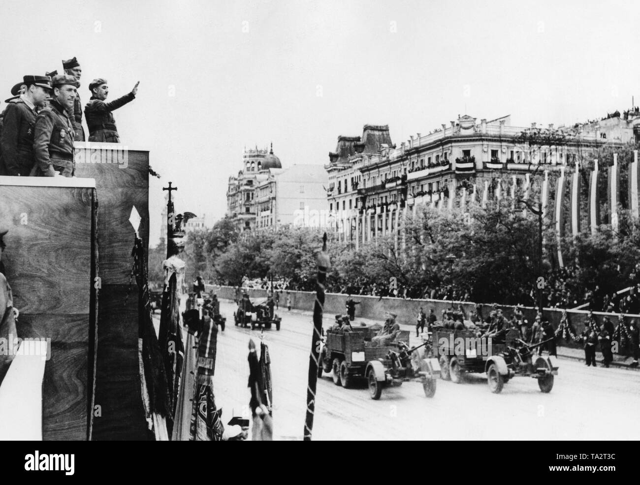 Photo du quartier de luxe de Paseo del la Castellana à Madrid au cours de la grande revue de la victoire des troupes national espagnol à Madrid le 19 mai 1939. Sur la gauche dans le bord de la photo, le Caudilo le général Francisco Franco (à droite avec son bras levé) et le général Freiherr Wolfram von Richthofen ainsi que d'autres hauts fonctionnaires de l'inspection sont la parade d'une scène. Sur la droite, une unité antiaérienne souille (Krupp L2 H143 tracteur avec 2cm flak 30). Banque D'Images