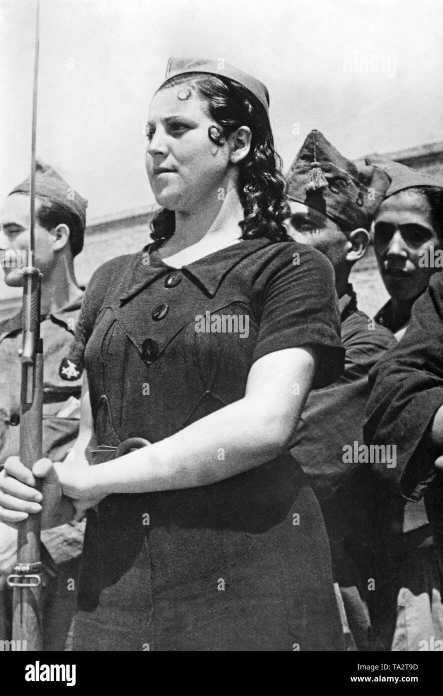 Photo d'un chasseur de femmes du 5e Régiment de la Milicias Populares de l'armée républicaine espagnole (Ejercito da da Republica Espanola) à Madrid, 1936. Le soldat porte une robe noire et est armé d'un Gewehr 98 avec une baïonnette. Dans l'arrière-plan, d'autres soldats en uniforme. Banque D'Images