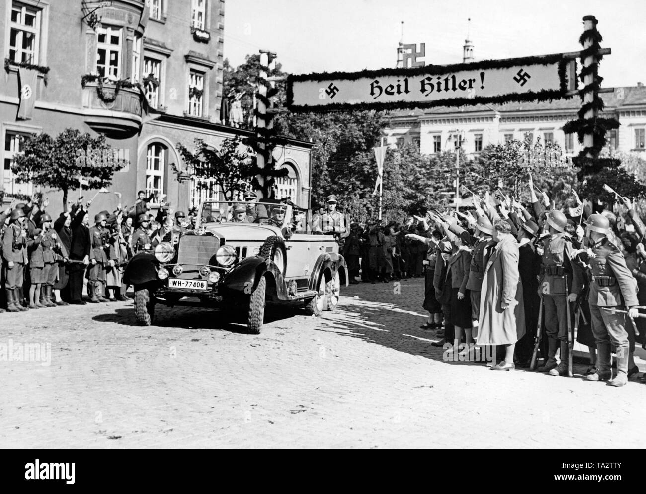 Adolf Hitler (avant gauche de la voiture) sur une visite à Jaegerndorf (aujourd'hui Krnov) le 7 octobre 1938, lors de l'occupation des Sudètes par l'Allemagne. La population reçoit lui gaiement en lui donnant le salut nazi. Au-dessus de la rue, une bannière avec l'inscription : "Heil Hitler !" Banque D'Images
