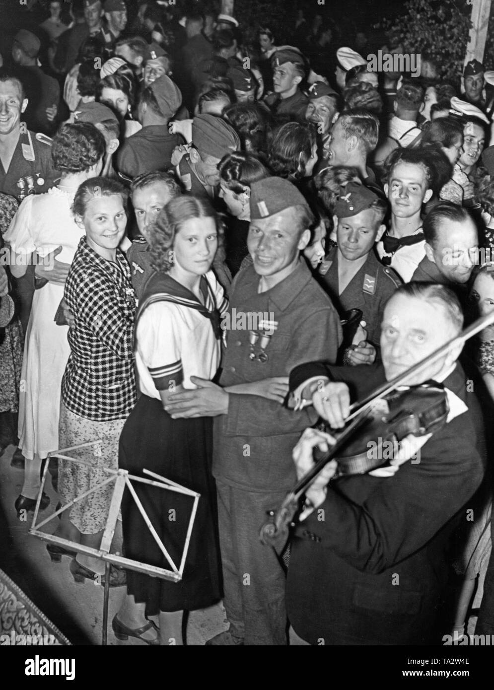 Photo d'un groupe de soldats de la légion Condor (l'armée et la force aérienne) et les femmes en uniforme de Berlin pendant une danse après la revue de la victoire de la troupe à Mitte (Berlin) dans la soirée du 6 juin 1939, à Doeberitz. Le joyeux bivouac était organisée par la Légion et le NSG "Kraft durch Freude" (organisation Nazie "force par la joie"). Il y avait un feu de bivouac, des spectacles en plein air et feu d'artifice. Dans l'avant-plan est un violoniste. Banque D'Images