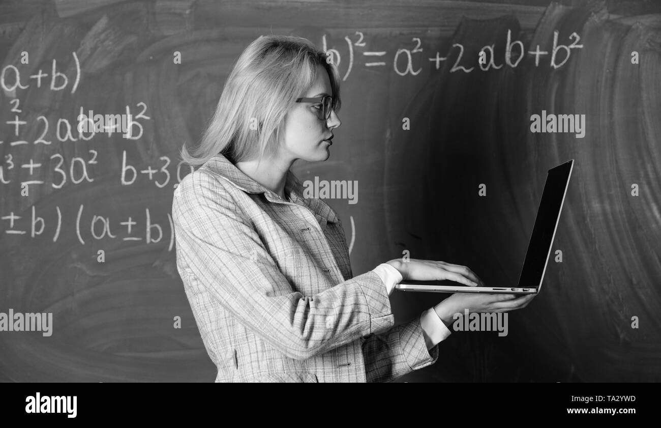 L'apprendre de manière simple. Enseignante portent des lunettes est titulaire d'ordinateur portable Internet surf. Les technologies numériques concept. Dame intelligente smart éducateur avec ordinateur portable moderne recherche d'informations d'arrière-plan du tableau. Banque D'Images