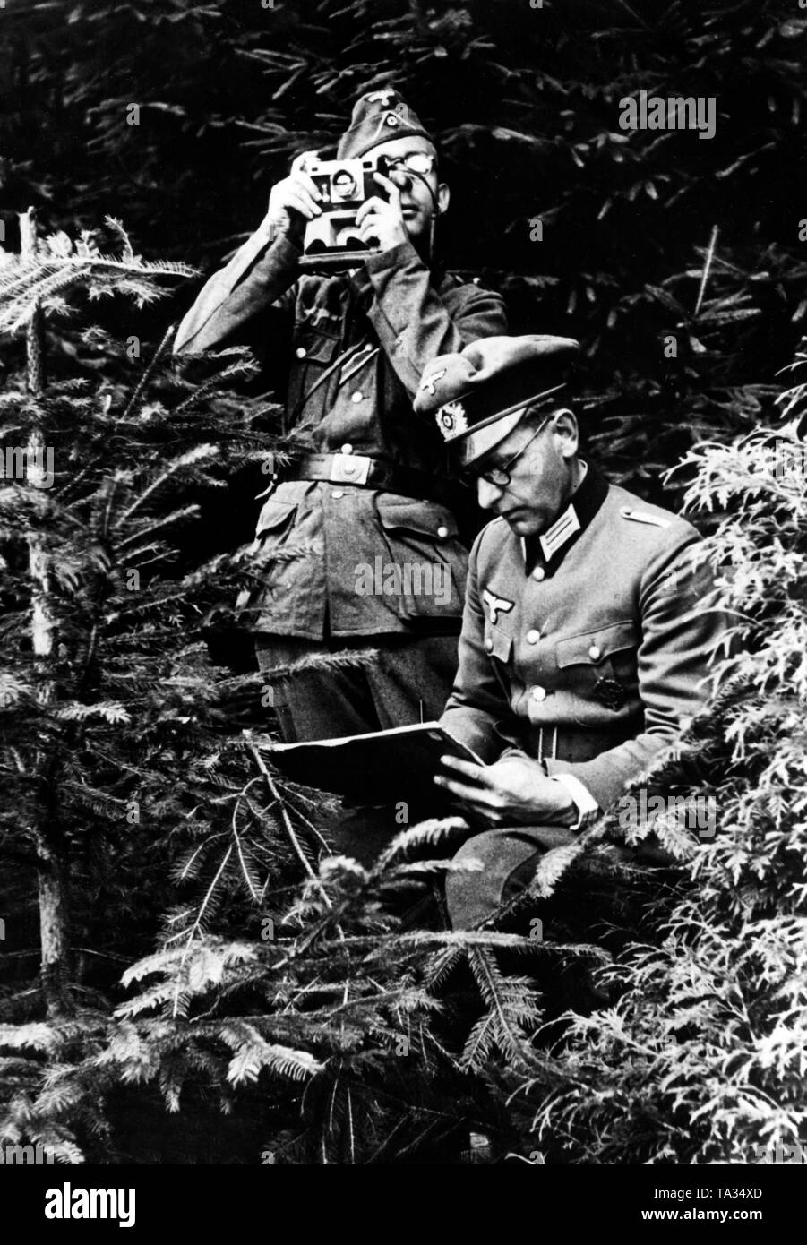 Deux correspondants de guerre de la Luftwaffe (Armée de l'air) d'une entreprise de propagande se déguisent en forêt. L'un d'entre eux teste sa caméra, l'autre écrit un rapport. Banque D'Images