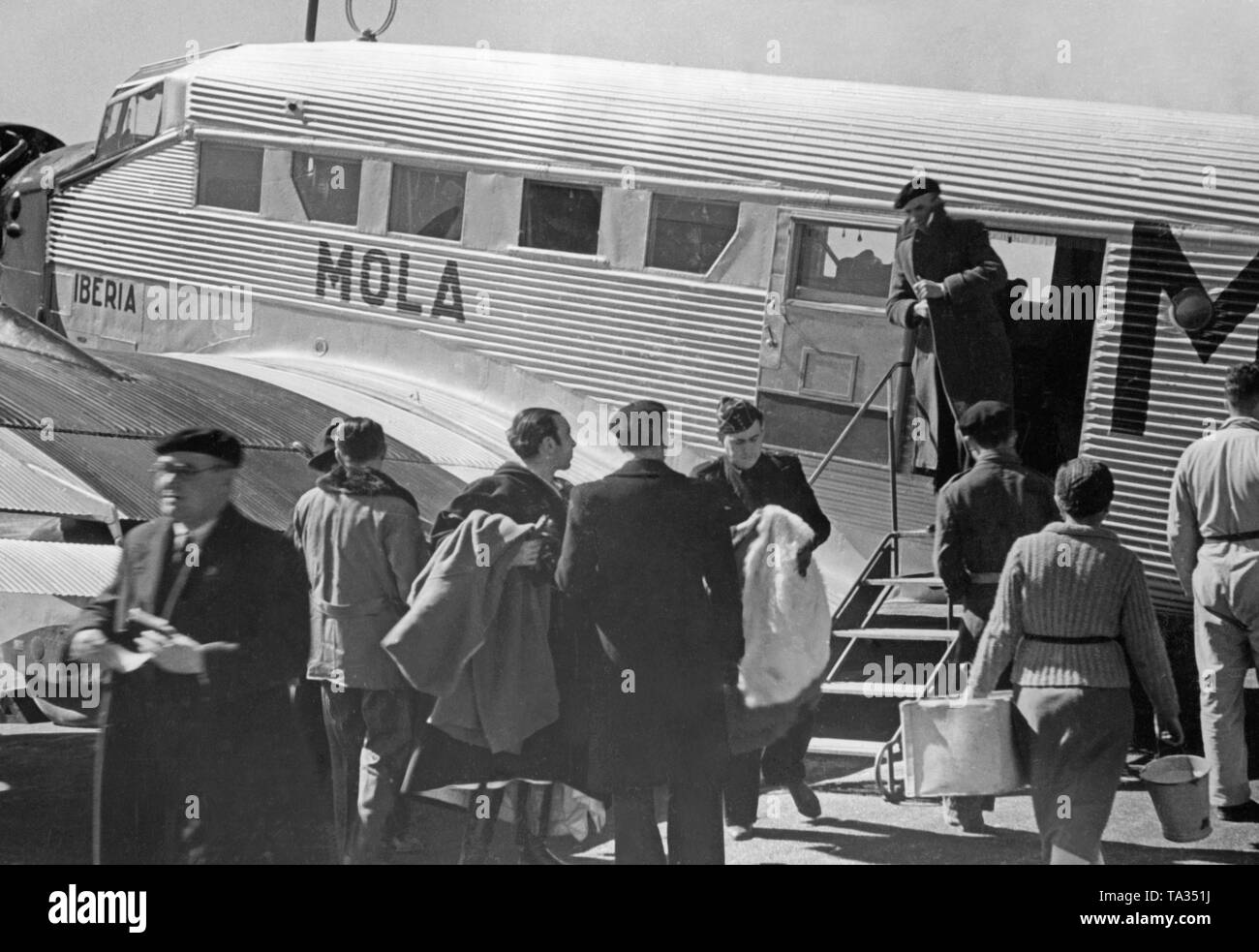 Photo d'un Junkers Ju 52 allemand de la compagnie aérienne espagnole Iberia 1939 à l'aéroport de Salamanque, Castille et Leon, Espagne, à travers les fenêtres de la nouvelle aérogare. Soldats et civils sont de descendre de l'avion. La machine est nommé 'ola', après que le général Emilio Mola Vidal (mort en 1937), l'un des dirigeants du soulèvement du Général Francisco Franco. Pendant la guerre civile, la Deutsche Lufthansa et l'Ibérie (fondée en 1927) a effectué des vols principalement avec les pilotes allemands dans la zone nationale espagnole à partir de 1937. L'aéronef ont été fournies par la Deutsche Lufthansa AG. Banque D'Images