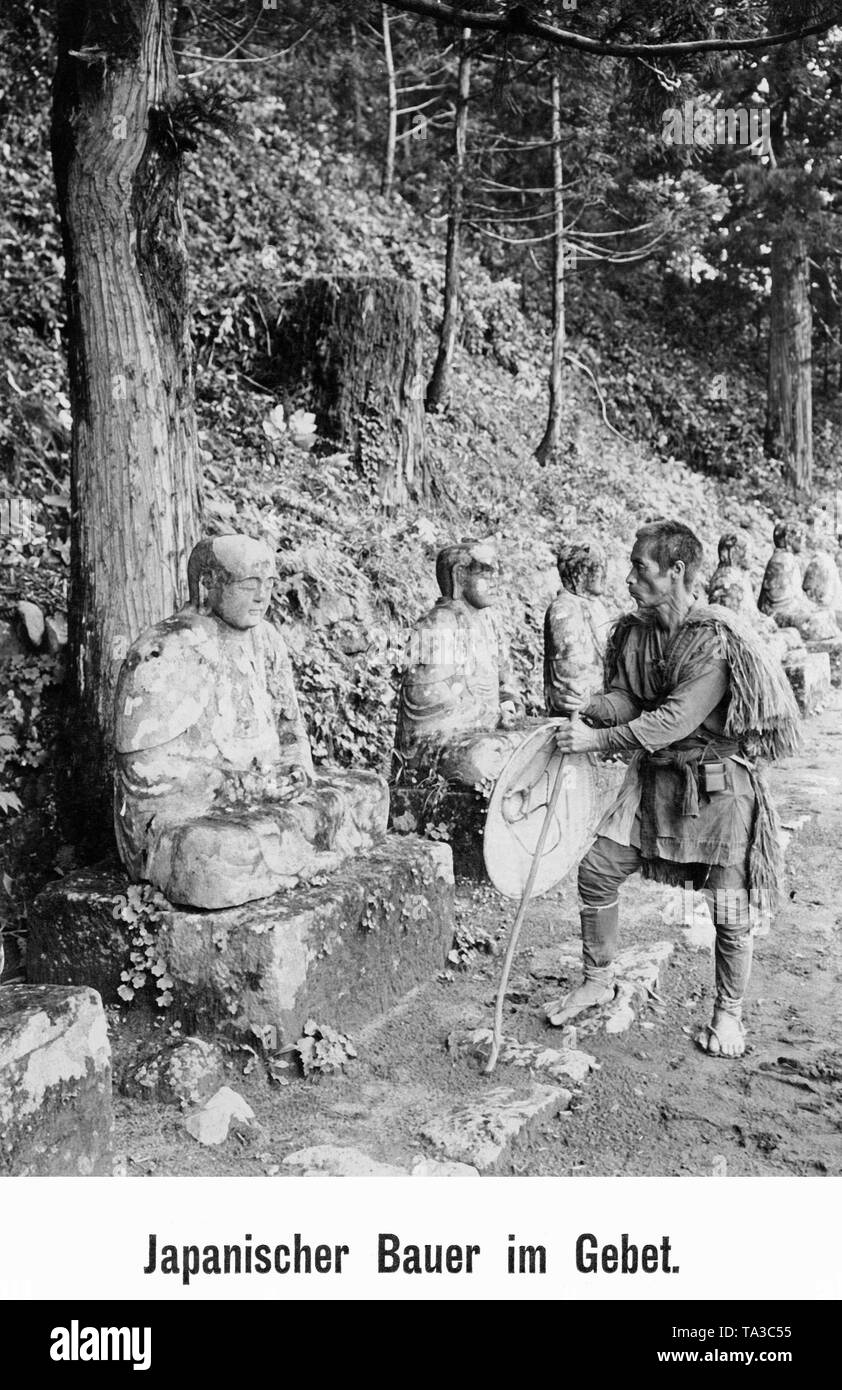 Un agriculteur japonais, devant une statue et prie. Il tient un bâton et un chapeau de paille dans sa main. Banque D'Images