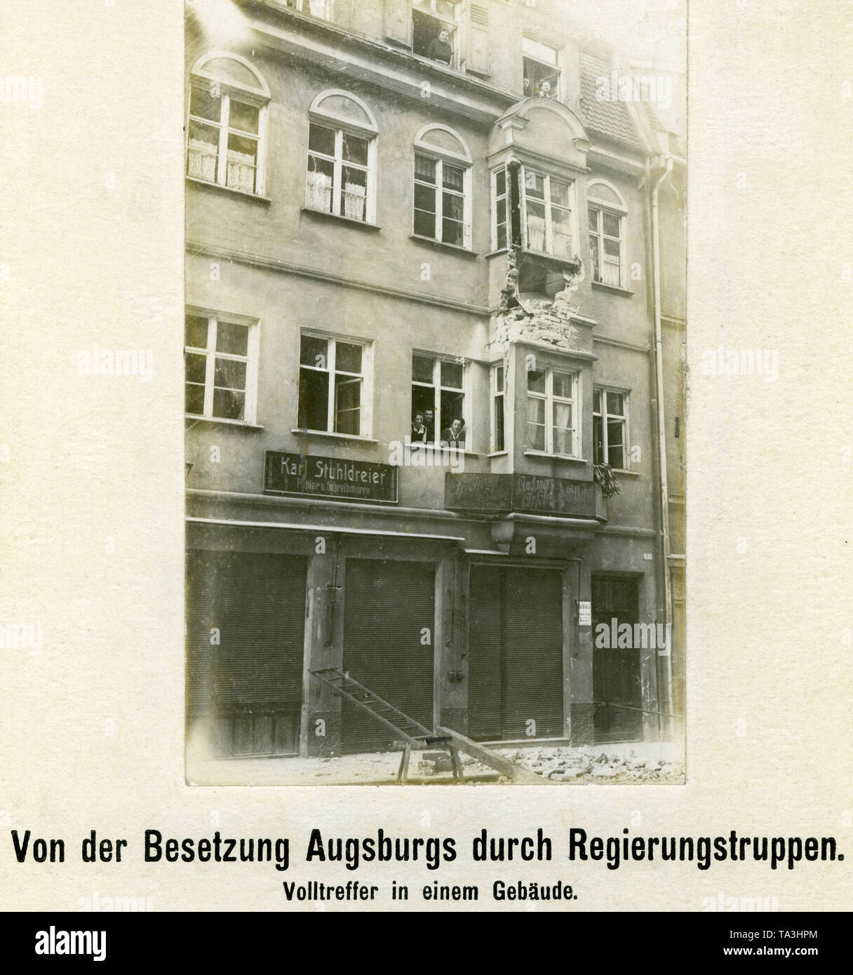 La photo montre un bâtiment endommagé par un succès à Augsbourg après l'occupation par les troupes gouvernementales sur Pâques 1919 (appelé "Pâques sanglantes" par l'Augsburgs). Le photographe montre résidents depuis leurs fenêtres. Banque D'Images