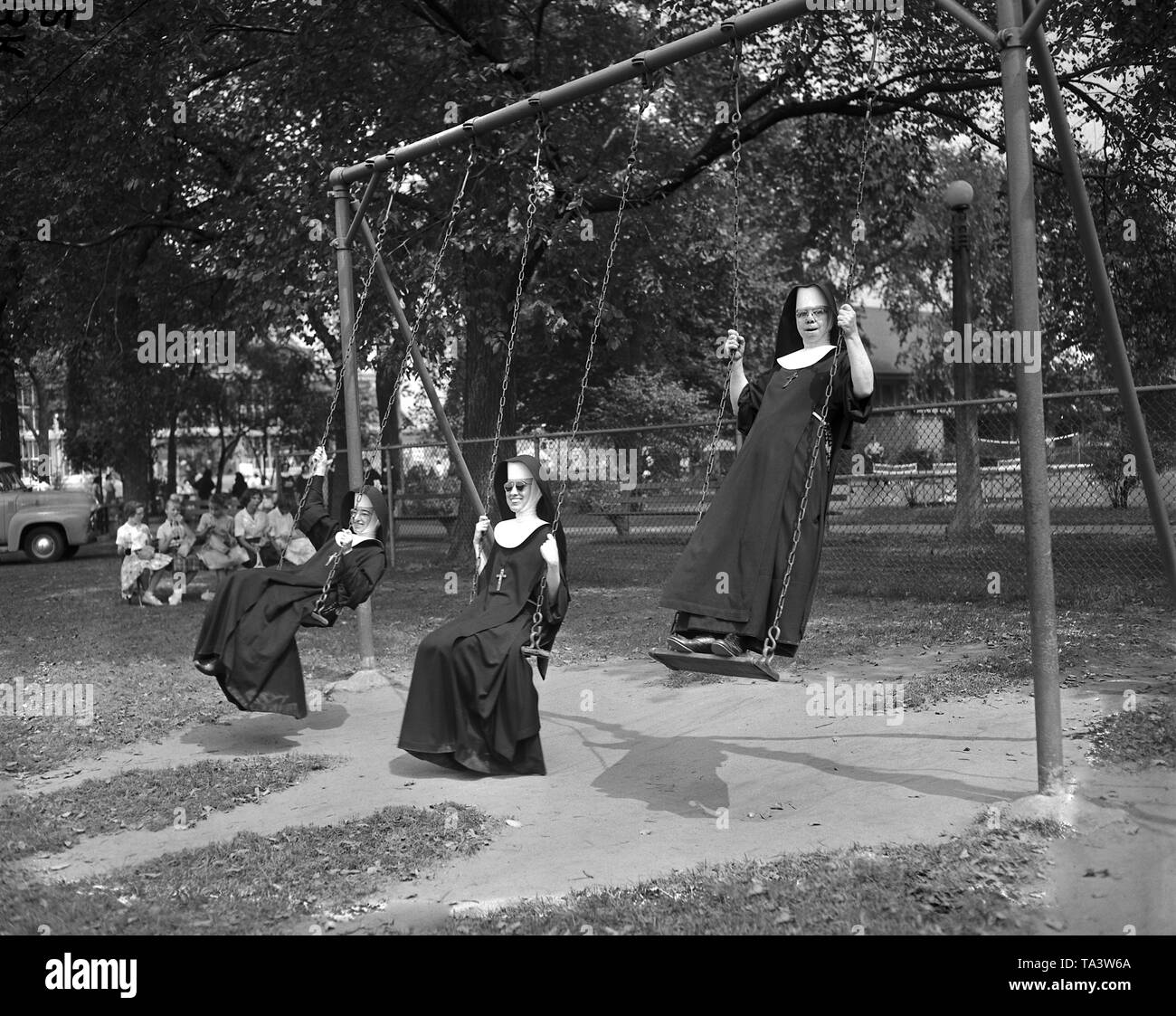 Trio de moniales s'amusant swinging sur balançoire dans un parc, 1960. Banque D'Images
