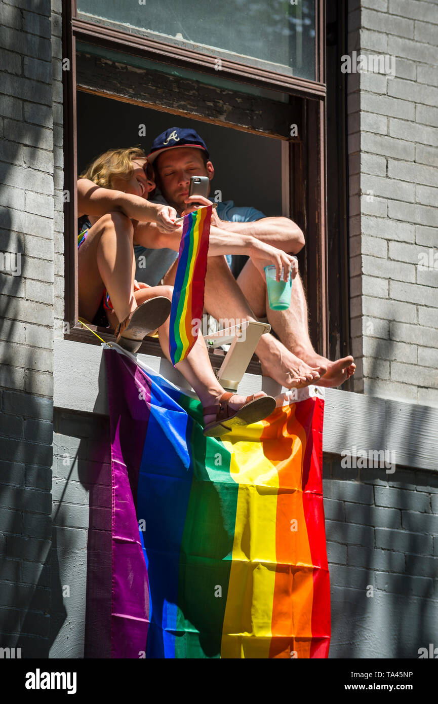 NEW YORK - 25 juin 2017 : Drapeaux et arcs-en-ciel vague partisans prendre des autoportraits d'un appartement d''une fenêtre donnant sur la Gay Pride Parade annuelle. Banque D'Images