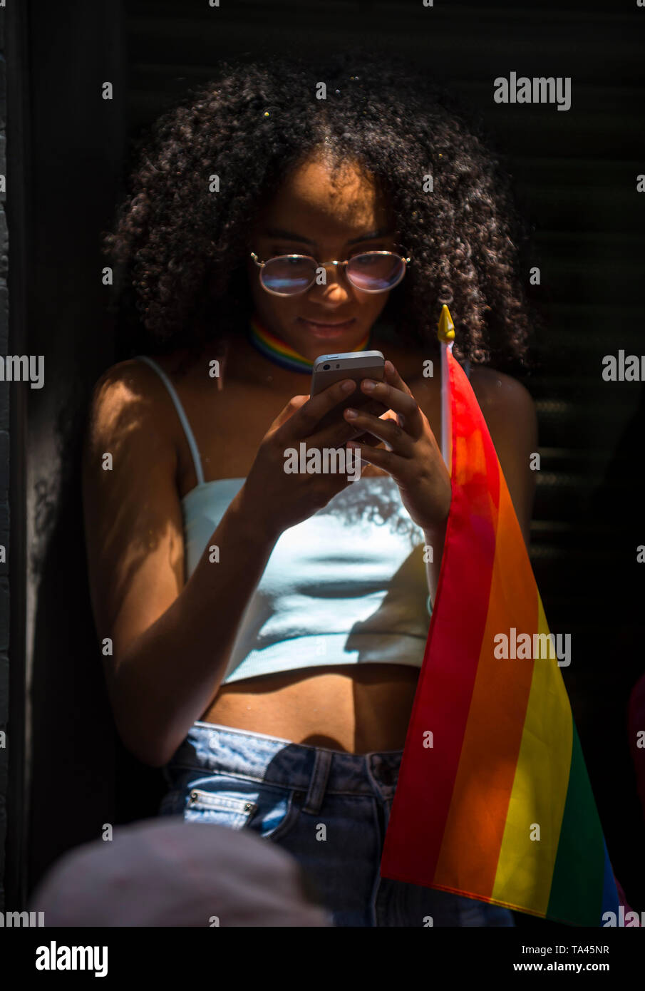 NEW YORK - 25 juin 2017 : Supporter avec le drapeau arc-en-ciel consulte ses médias sociaux sur son téléphone dans la Gay Pride Parade annuelle. Banque D'Images