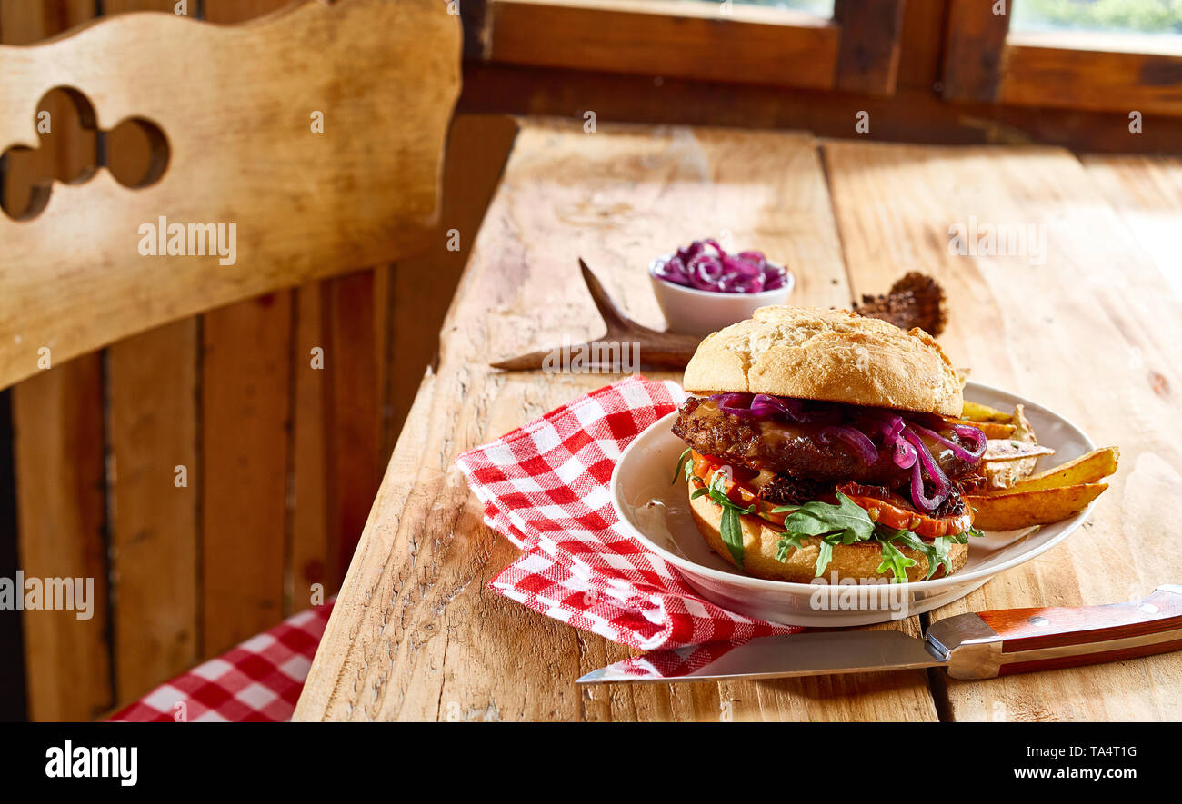Spécialité de gibier sauvage savoureux burger de boeuf sur un petit pain  croustillant avec les quartiers de pommes de terre servis sur une table  rustique avec des carreaux blancs et rouges à