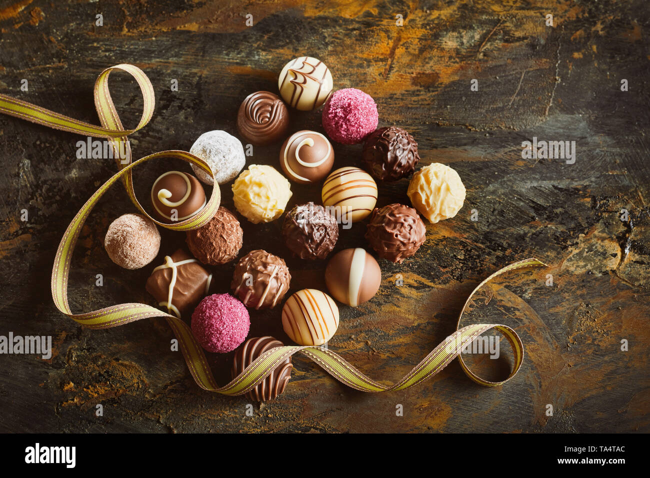 L'affichage du luxe élégant pralinés chocolat disposés en rectangle avec un ruban d'or tourbillonnant sur bois rustique vu de passage Banque D'Images