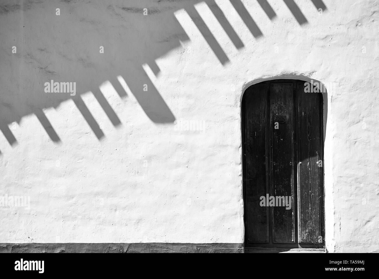 Un mur blanc avec des ombres et un toit porte en bois à la Purisima Mission à Lompoc, en Californie. Banque D'Images