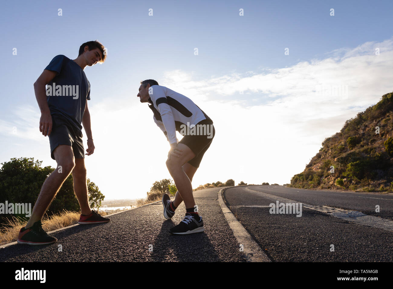 Père et fils faisant exercice s'étendant sur route Banque D'Images