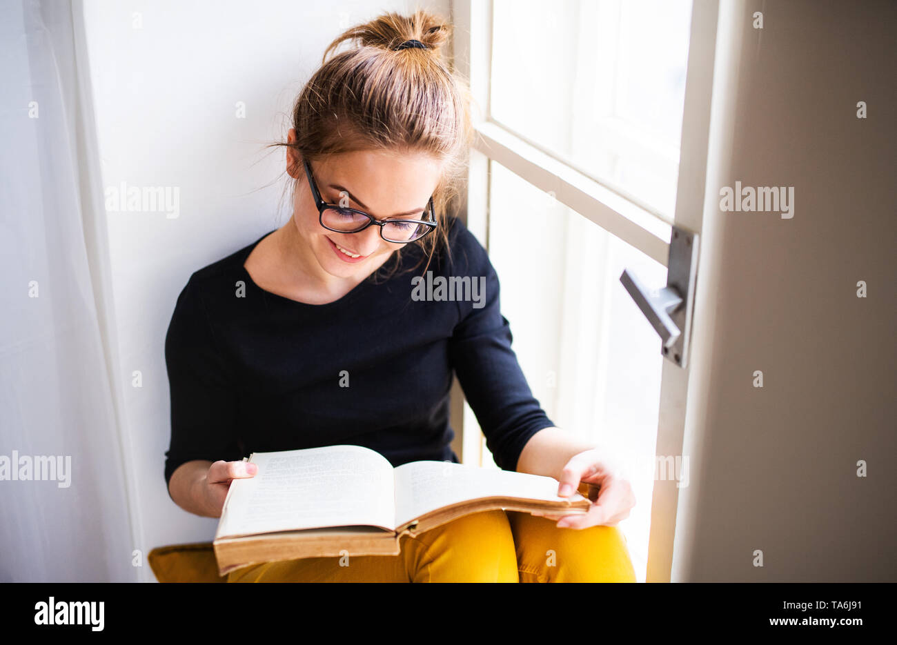 Une jeune étudiante avec livre assis sur un rebord de fenêtre, l'étude. Banque D'Images