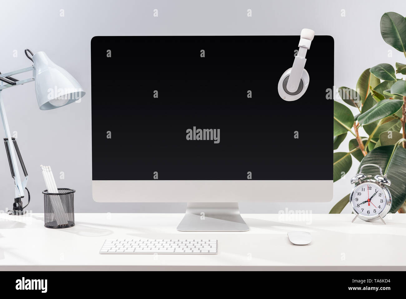 Lieu de Travail avec casque sur l'écran d'ordinateur, lampe et papeterie sur table blanc sur fond gris Banque D'Images