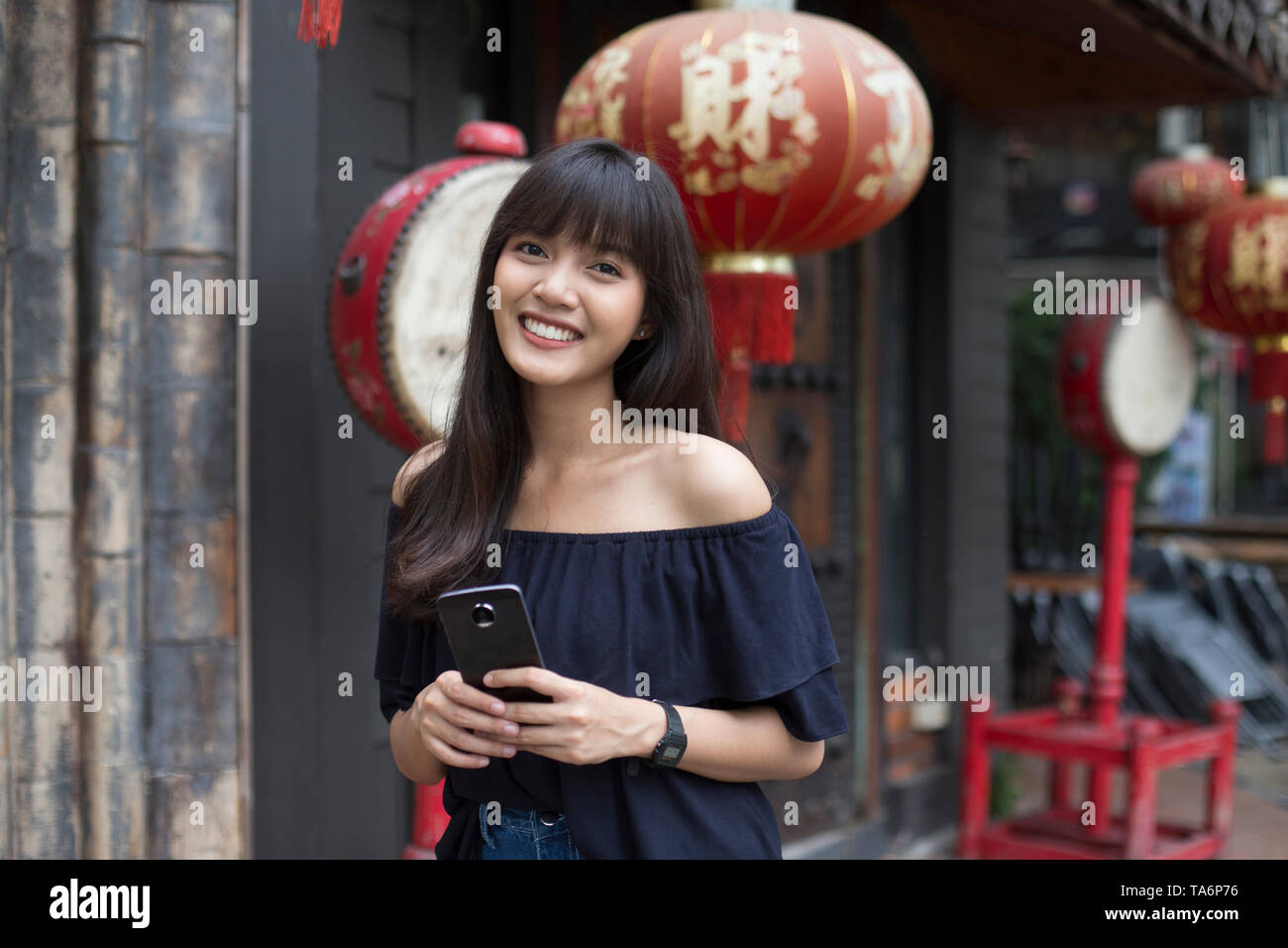 Portrait of smiling young asian woman holding smart phone in front of Chinese Restaurant Banque D'Images