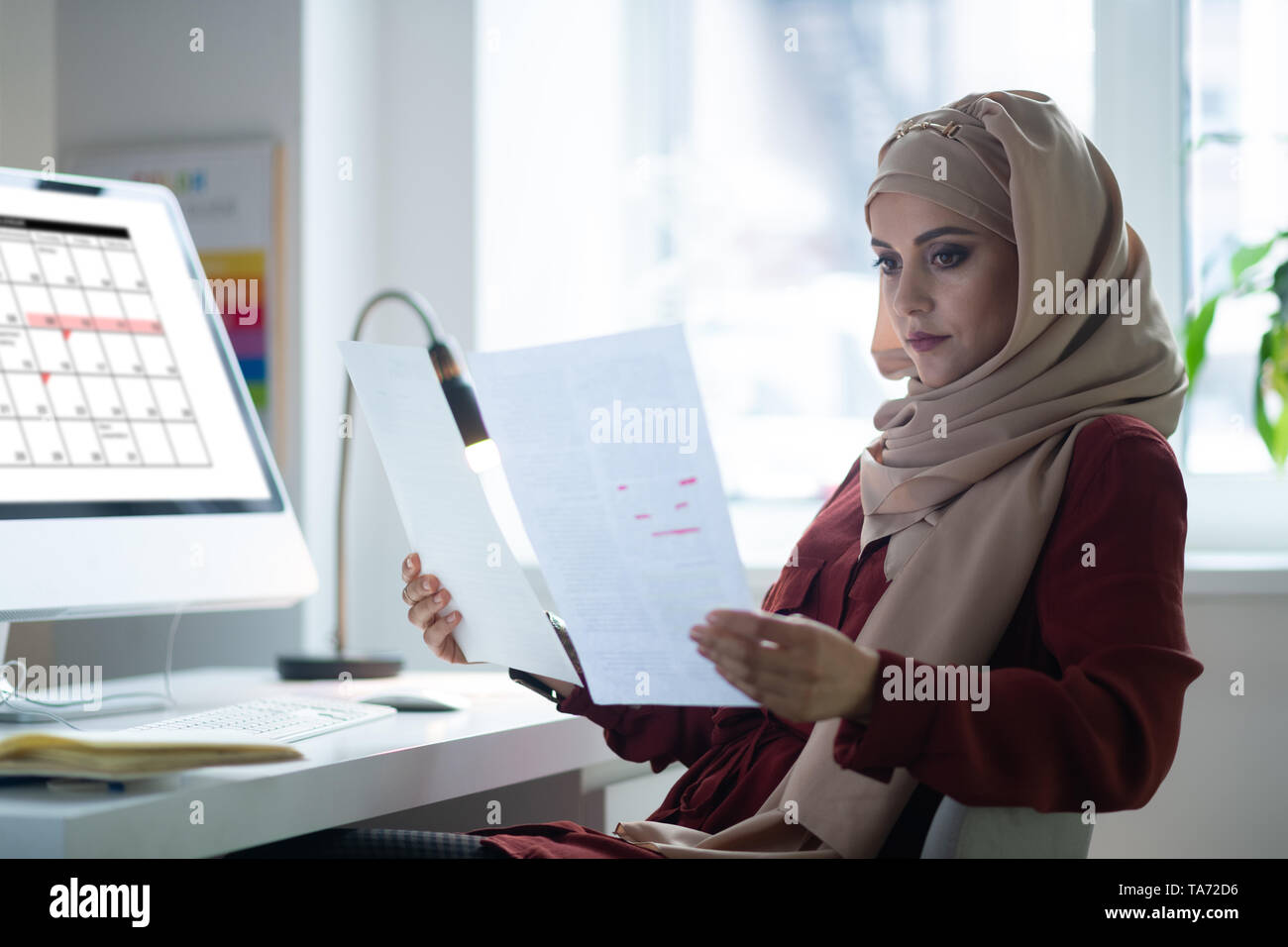 Enseignant aux yeux noirs portant le hijab assis près de l'ordinateur Banque D'Images