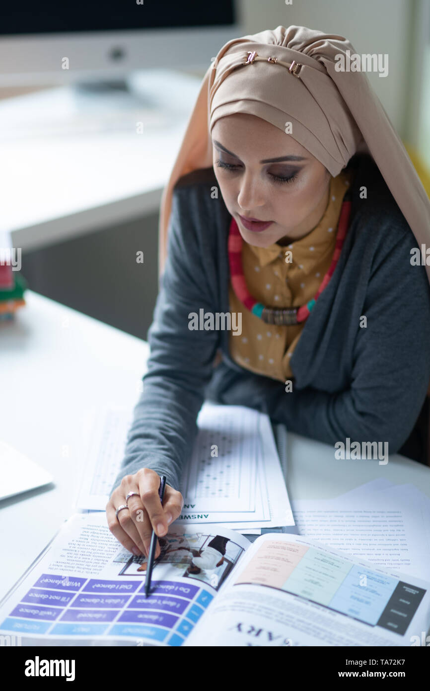 Jeune enseignante musulmane la lecture du texte tout en corrigeant les tests Banque D'Images