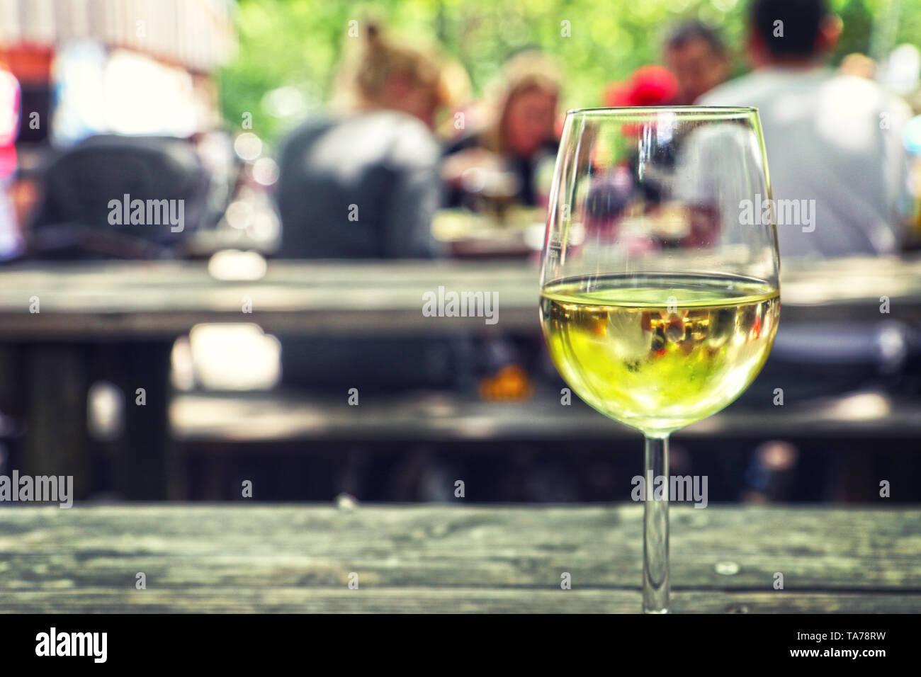En sirotant un verre de vin blanc à l'extérieur sur un banc avec des personnes floues en arrière-plan Banque D'Images