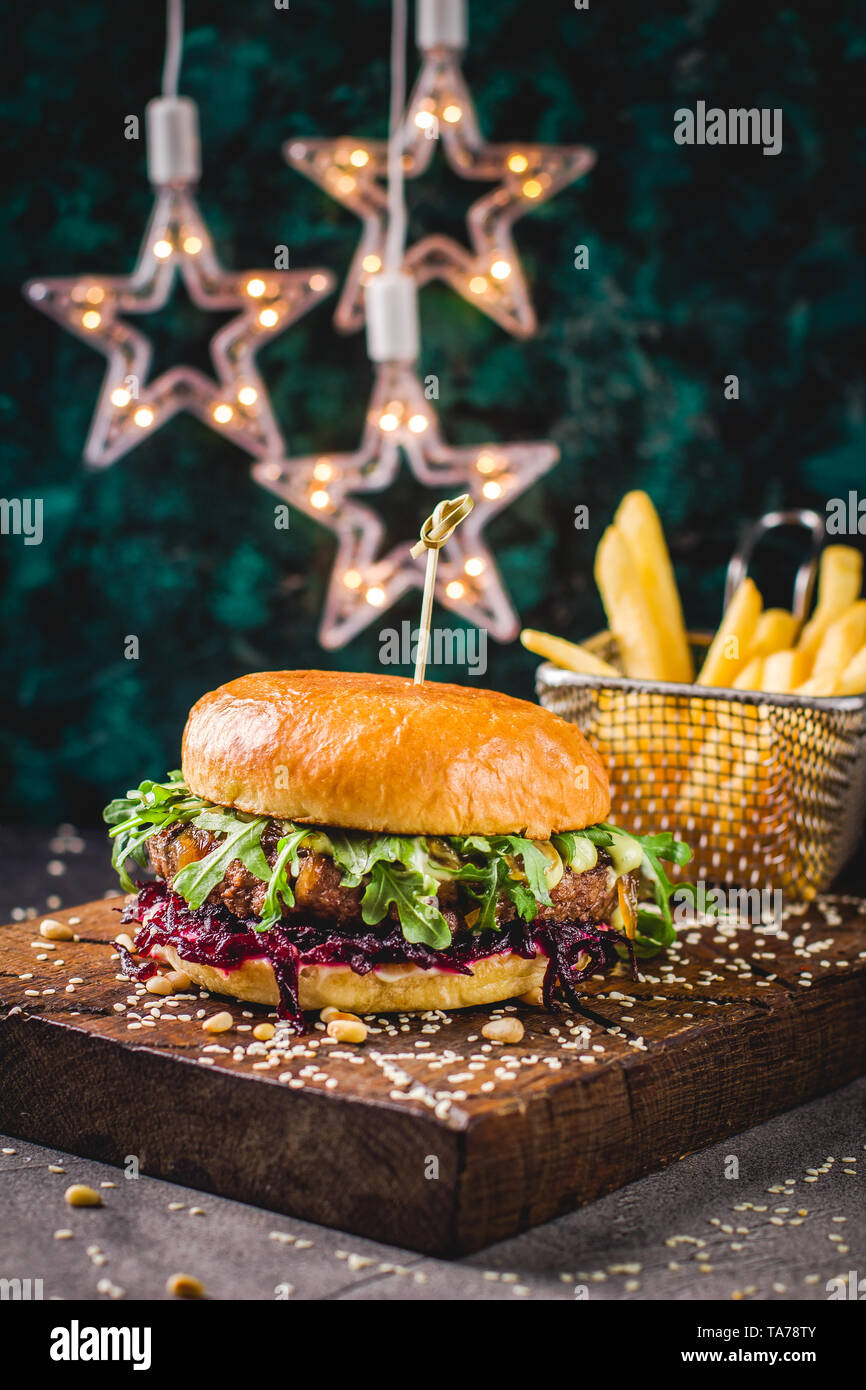 Close-up of tasty burger de boeuf, oignons caramélisés et de betterave, roquette et sauce wasabi et frites sur une planche à découper en bois. L'alimentation de rue, Banque D'Images