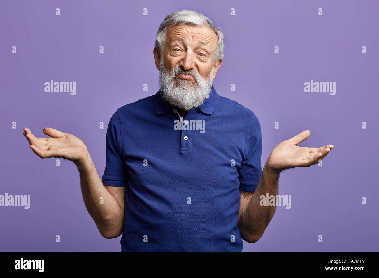 Vieil homme barbu exprime clueless avec bras levés regardant la caméra.isolé sur fond bleu. Ça ne me dérange pas. Il ne s'inquiète pas de moi.Je n'ai pas k Banque D'Images