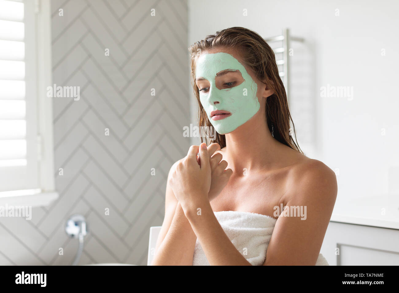 Femme sérieuse avec masque facial assis dans la salle de bains Banque D'Images