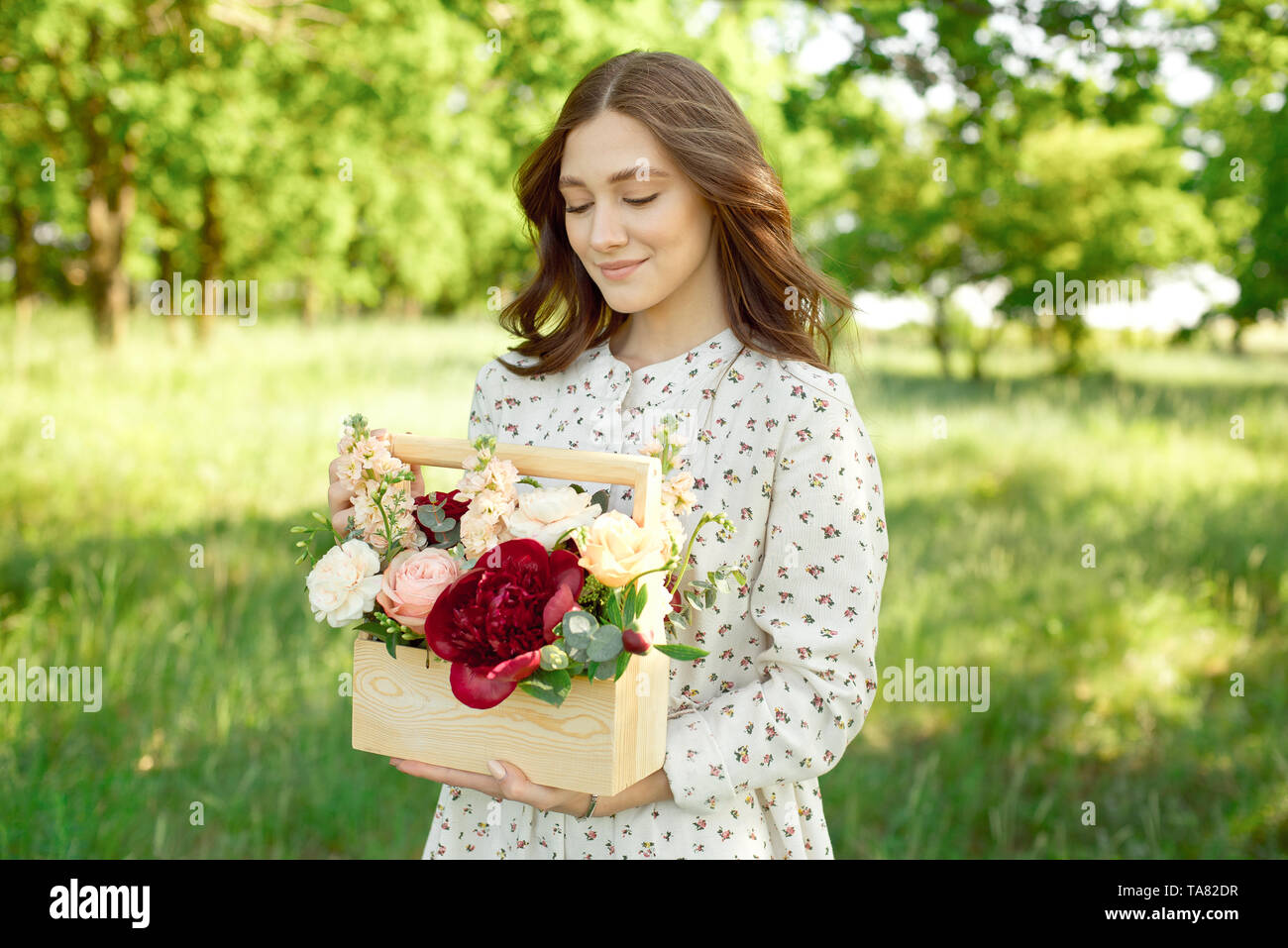 La moitié d'un portrait positif de charme femme vêtue de longues robes blanches avec un sourire heureux sur le fond d'un pré vert dans les mains de Banque D'Images