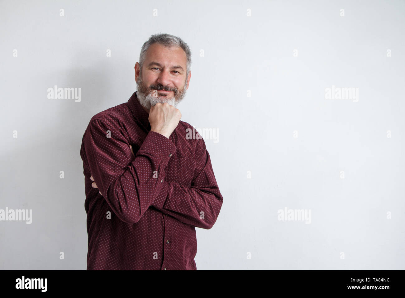 Portrait de mi-longueur d'un homme barbu aux cheveux gris dans un bourgogne chemise sur un fond blanc. Banque D'Images