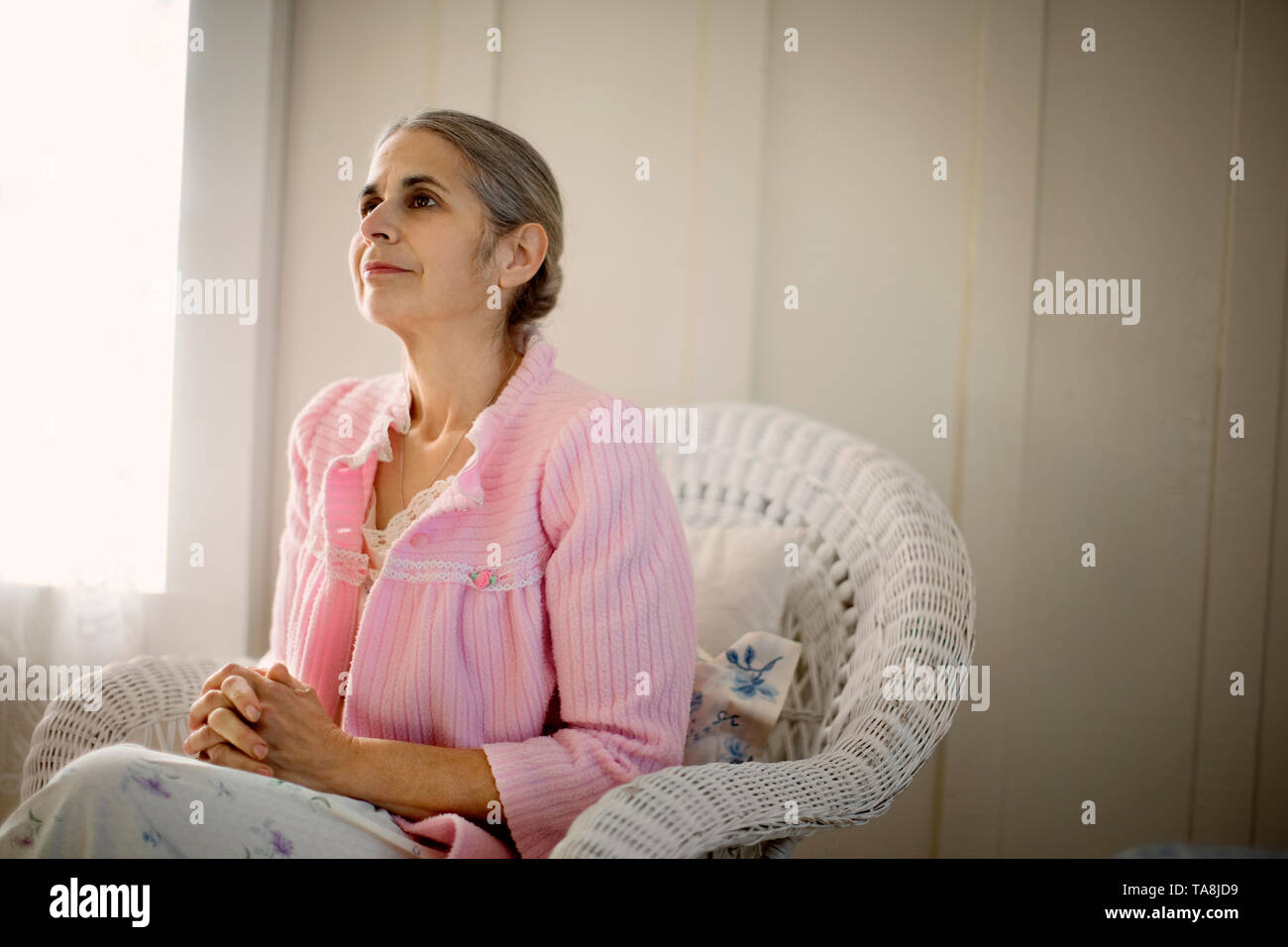 Senior woman sitting contemplatif dans un fauteuil avec ses mains jointes. Banque D'Images