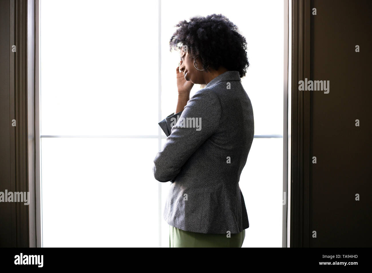 Silhouette d'un stressé black African American businesswoman smiling et réfléchir aux problèmes et l'échec par la fenêtre du bureau. Elle l Banque D'Images