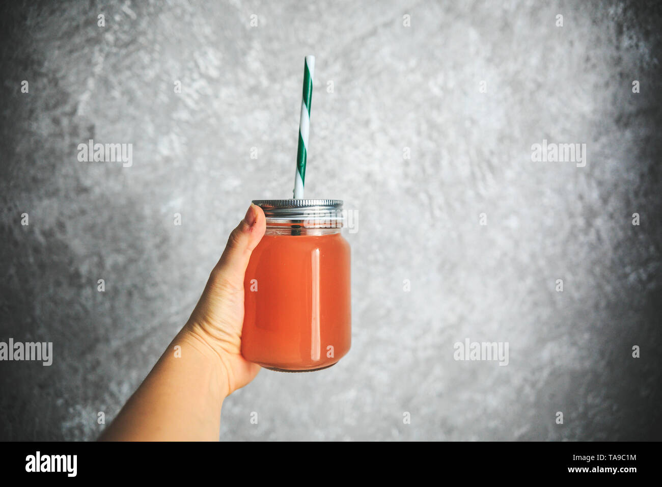 Le jus de pamplemousse dans le pot avec de la paille tenant dans la main sur le fond blanc et gris. Banque D'Images