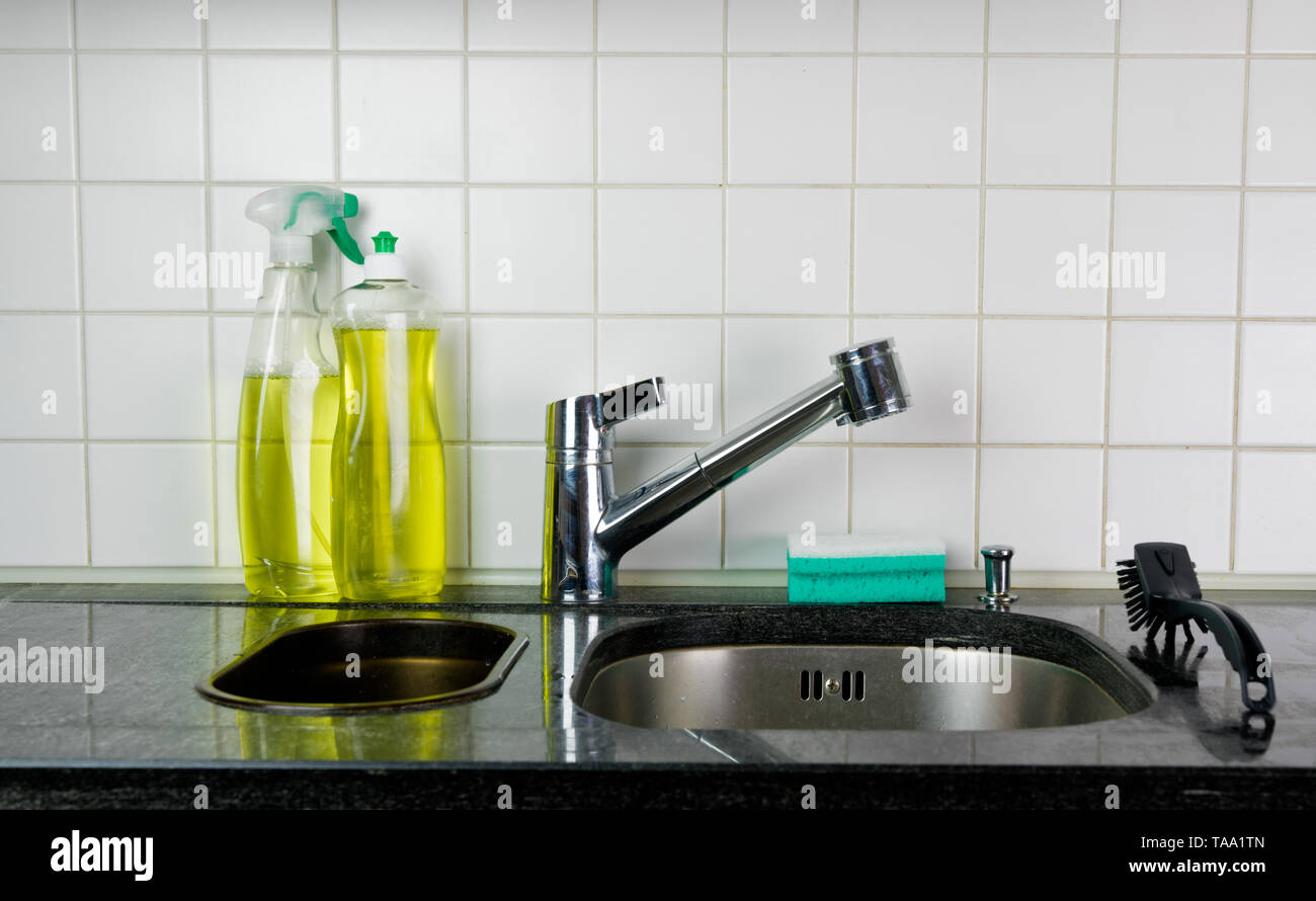 Et le robinet d'évier de cuisine avec une éponge et un pinceau sur un dessus de table en granit noir et jaune liquide vaisselle nettoyant cuisine et derrière Banque D'Images