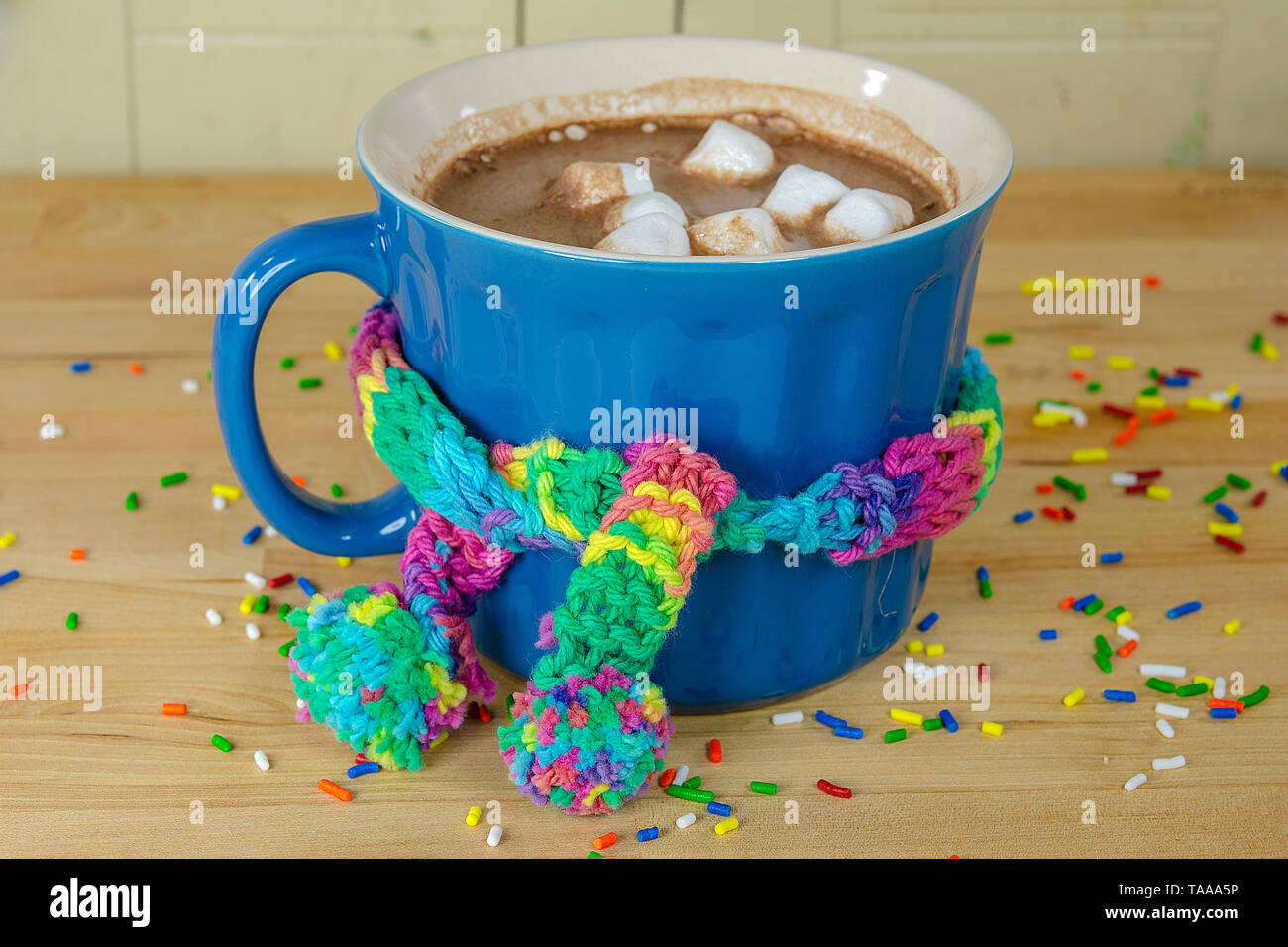 Boire un chocolat chaud avec tricot coloré foulard noué sur bleu mug sur la table en bois et arrose Banque D'Images