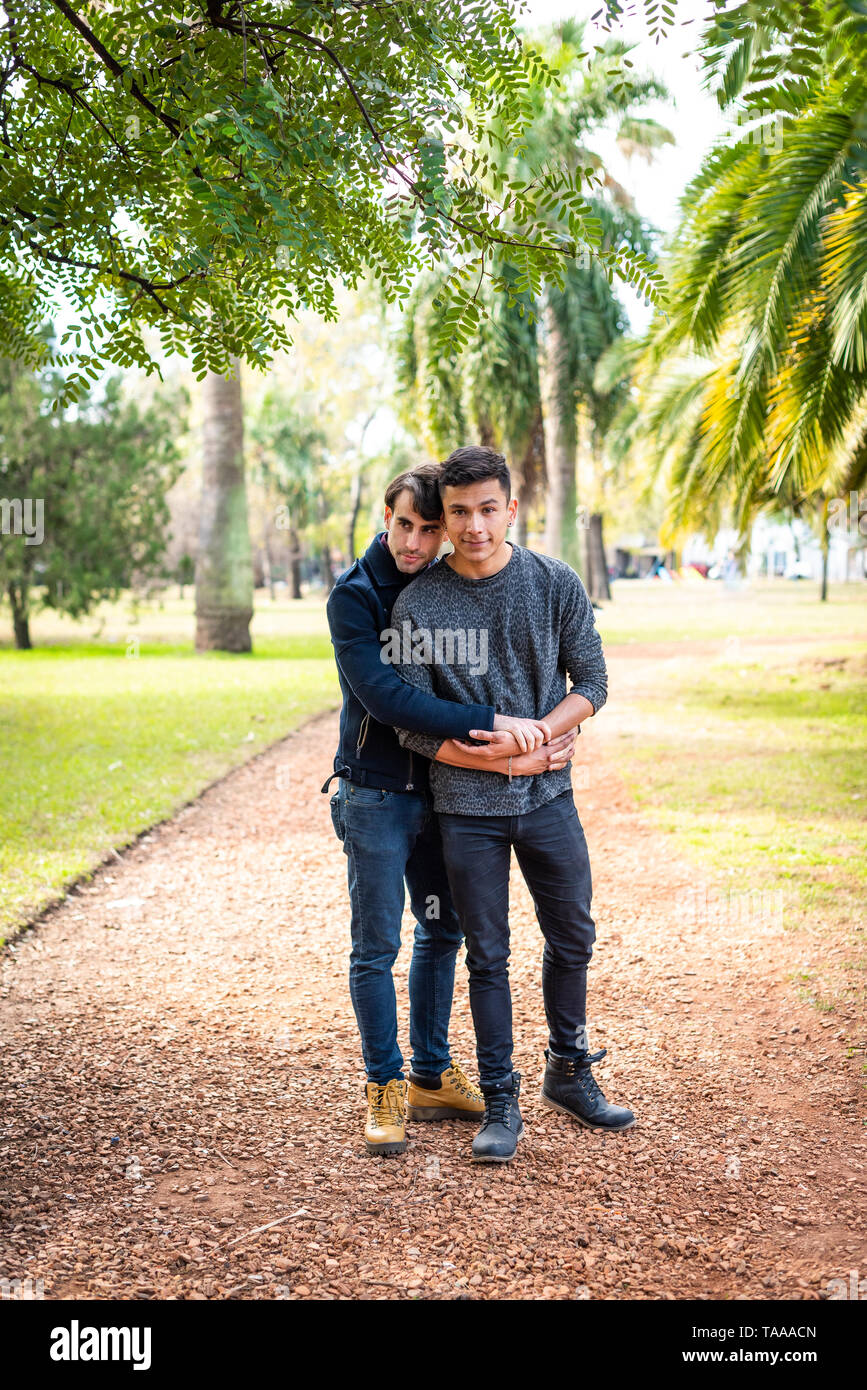 Les jeunes hommes homosexuels adultes élégant couple hugging at park eux-mêmes heureux et looking at camera Banque D'Images