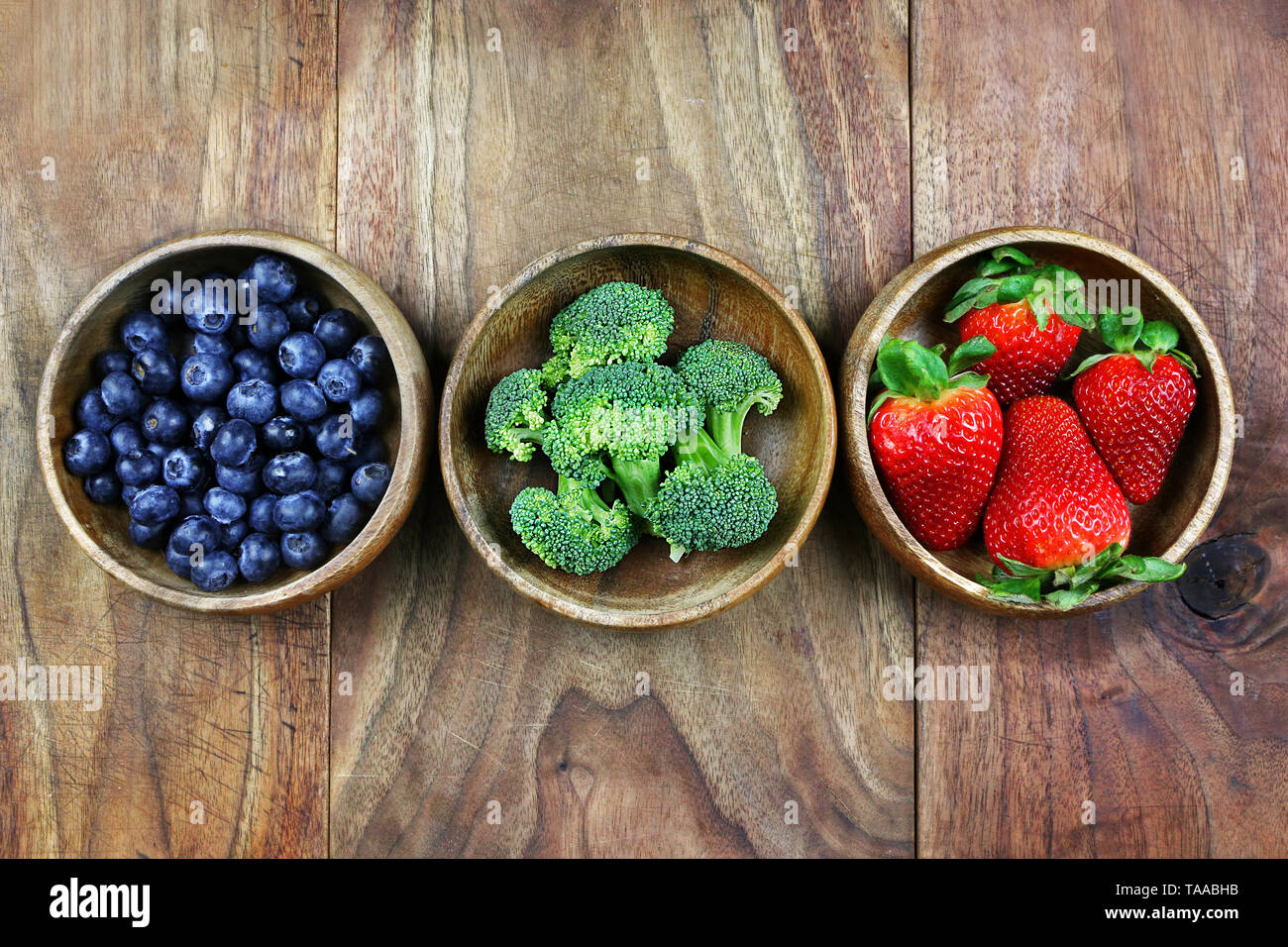 Trois petits bols en bois sont remplis de fruits et légumes frais, sains et assis sur une planche en bois rustique. Banque D'Images