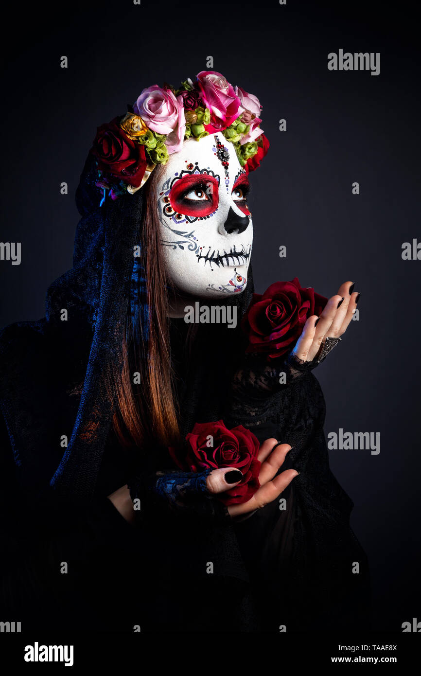 Fille avec crâne en sucre composent avec des fleurs rose pour célébrer le Jour des Morts à fond noir Banque D'Images