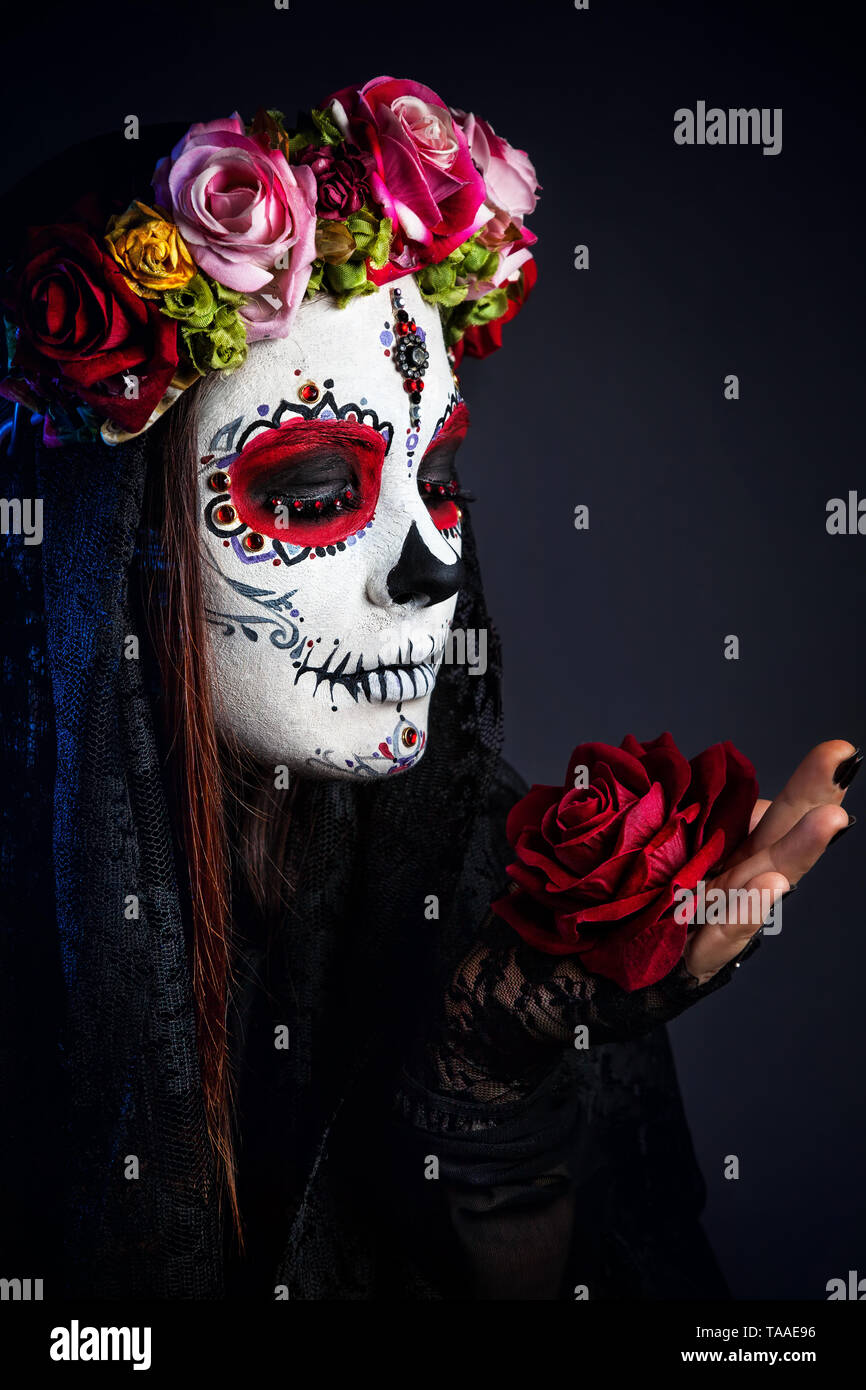Fille avec crâne en sucre composent avec fleur rose pour célébrer le Jour des Morts à fond noir Banque D'Images