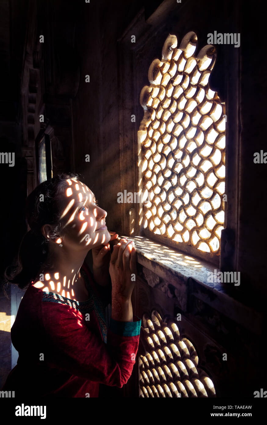 Femme en rouge sur le balcon du Penjab indien près de la fenêtre dans le musée du palais de la ville d'Udaipur, Rajasthan, Inde Banque D'Images