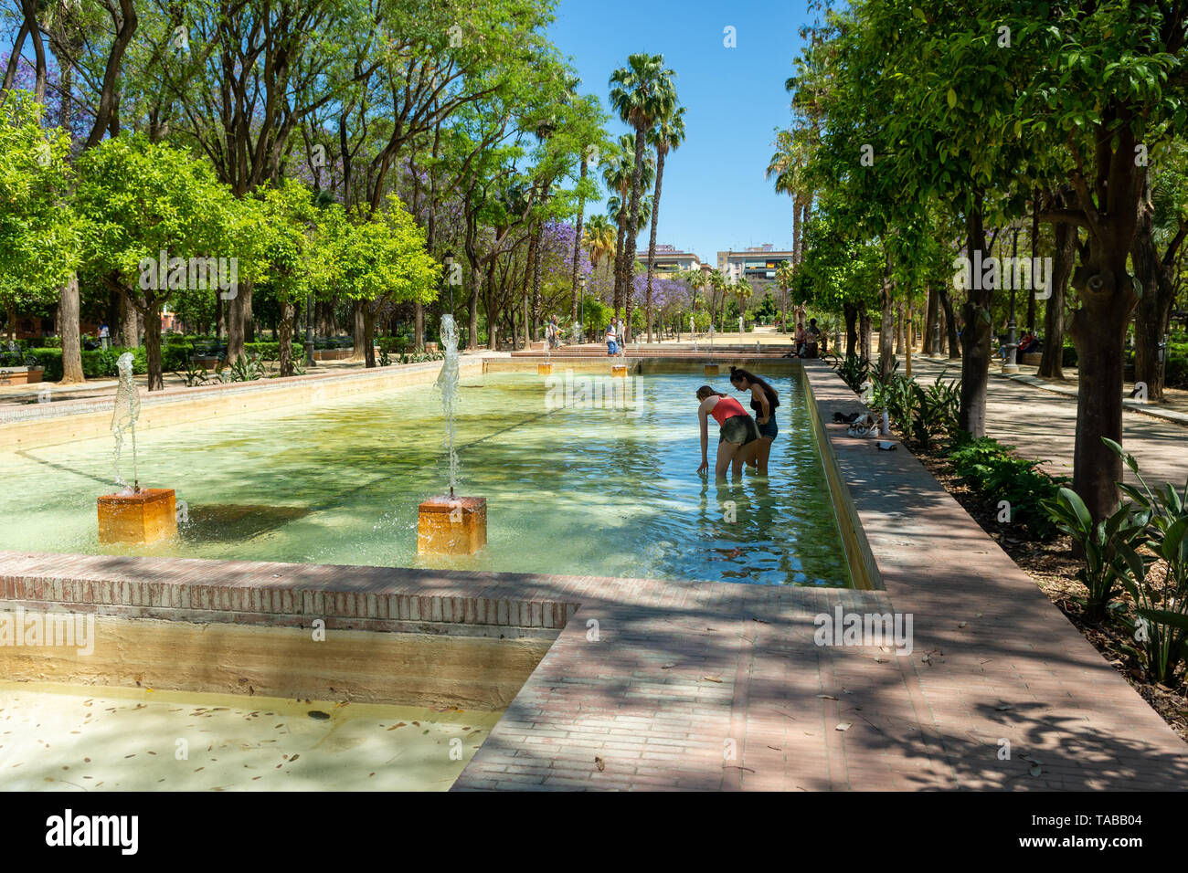 Deux jeunes femmes en phase de refroidissement sur une chaude journée à faible niveau de pagaie et fontaine d''eau, Prado de San Sebastian, Séville, Andalousie, Espagne Banque D'Images