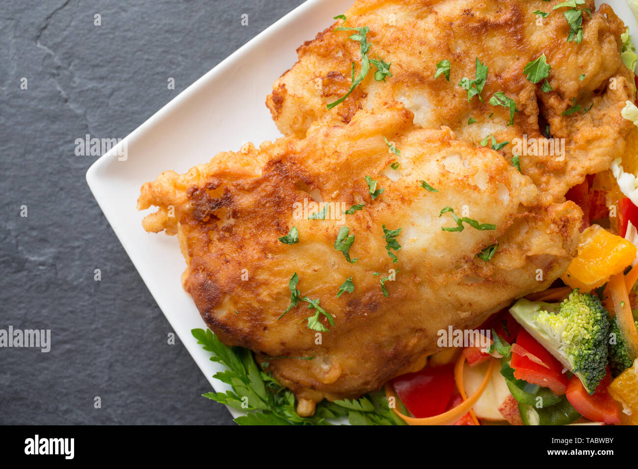 Deux épais filets de colin, Pollachius pollachius, qui ont été en grande friture pâte fait maison et servi avec des fruits et légumes crus. L'pollac Banque D'Images