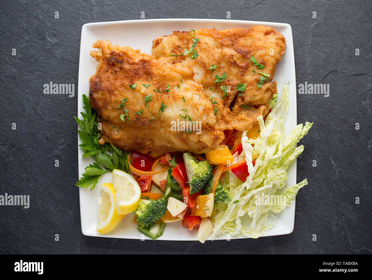 Deux épais filets de colin, Pollachius pollachius, qui ont été en grande friture pâte fait maison et servi avec des fruits et légumes crus. L'pollac Banque D'Images