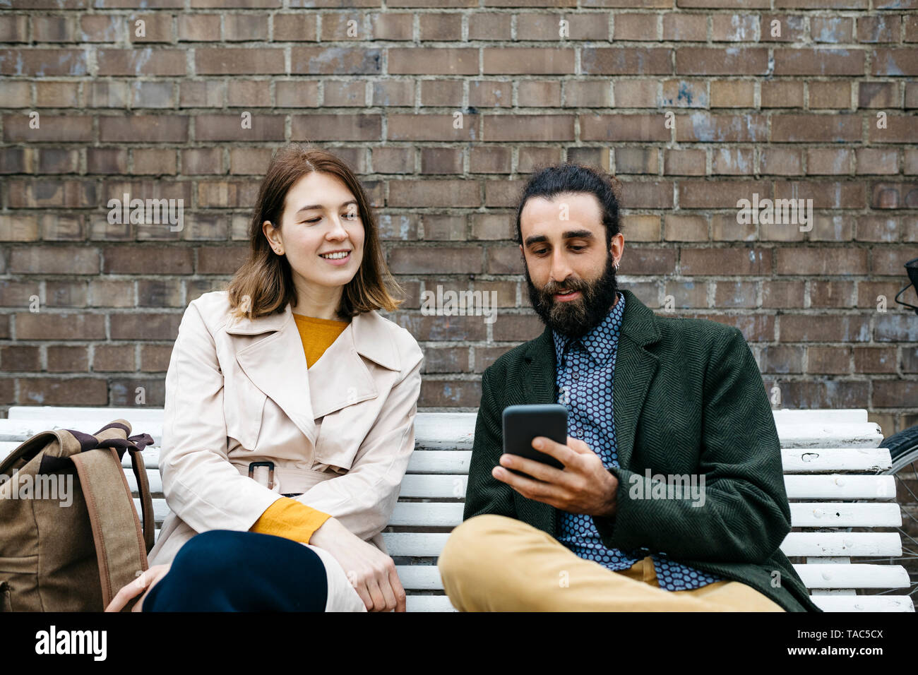 Couple assis sur un banc à un mur de briques partager cell phone Banque D'Images
