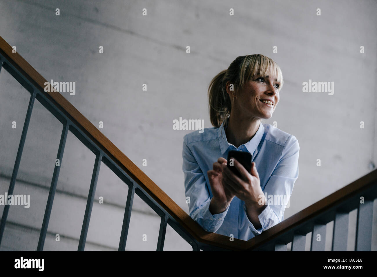 Businesswoman leaning on railing, using smartphone Banque D'Images