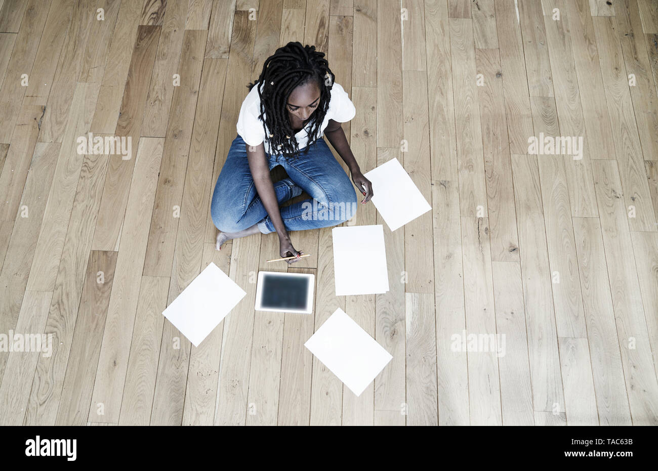 Femme assise sur le sol avec tablette numérique et des feuilles de papier vierges Banque D'Images