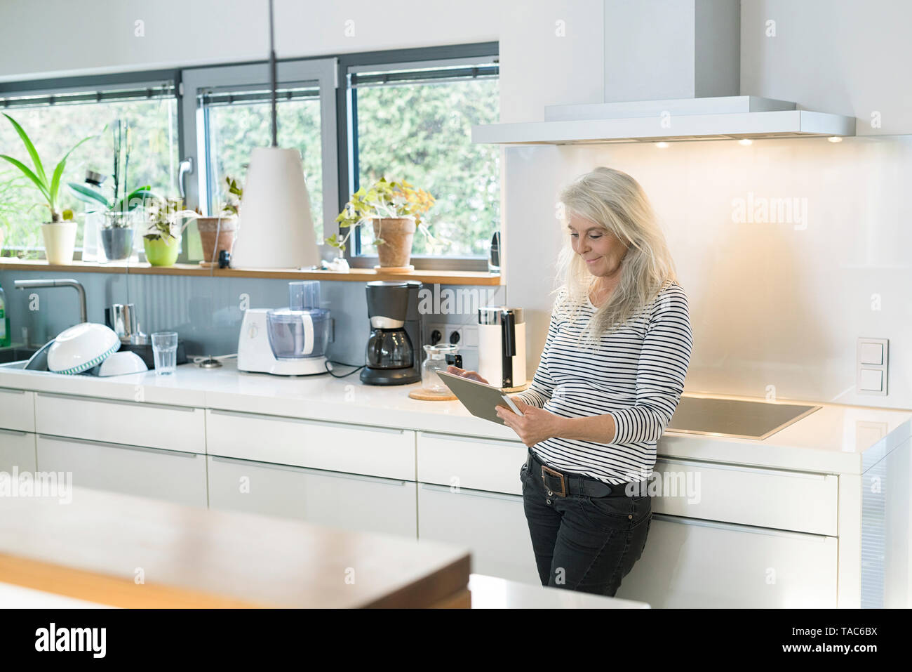 Content woman standing in kitchen using digital tablet Banque D'Images Content woman standing in kitchen using digital tablet Banque D'Images
