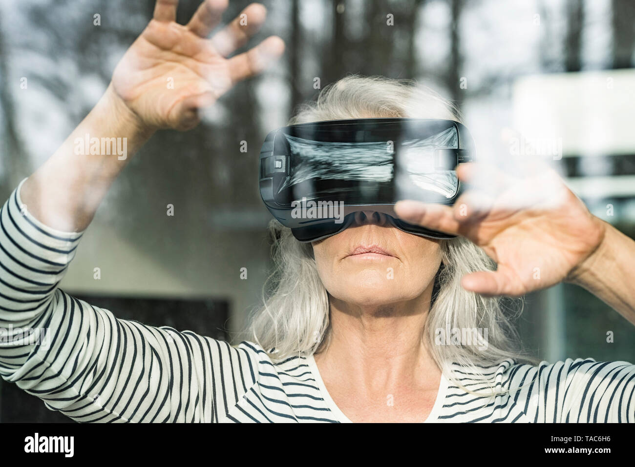 Portrait of mature femme derrière la vitre à l'aide de lunettes de réalité virtuelle Banque D'Images