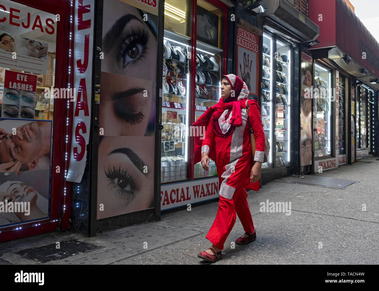 Une femme musulmane dans une robe aux couleurs vives et du hijab en passant devant un sourcil beauté sous le métro surélevé sur l'avenue Roosevelt à Jackson Heights, NEW YORK Banque D'Images
