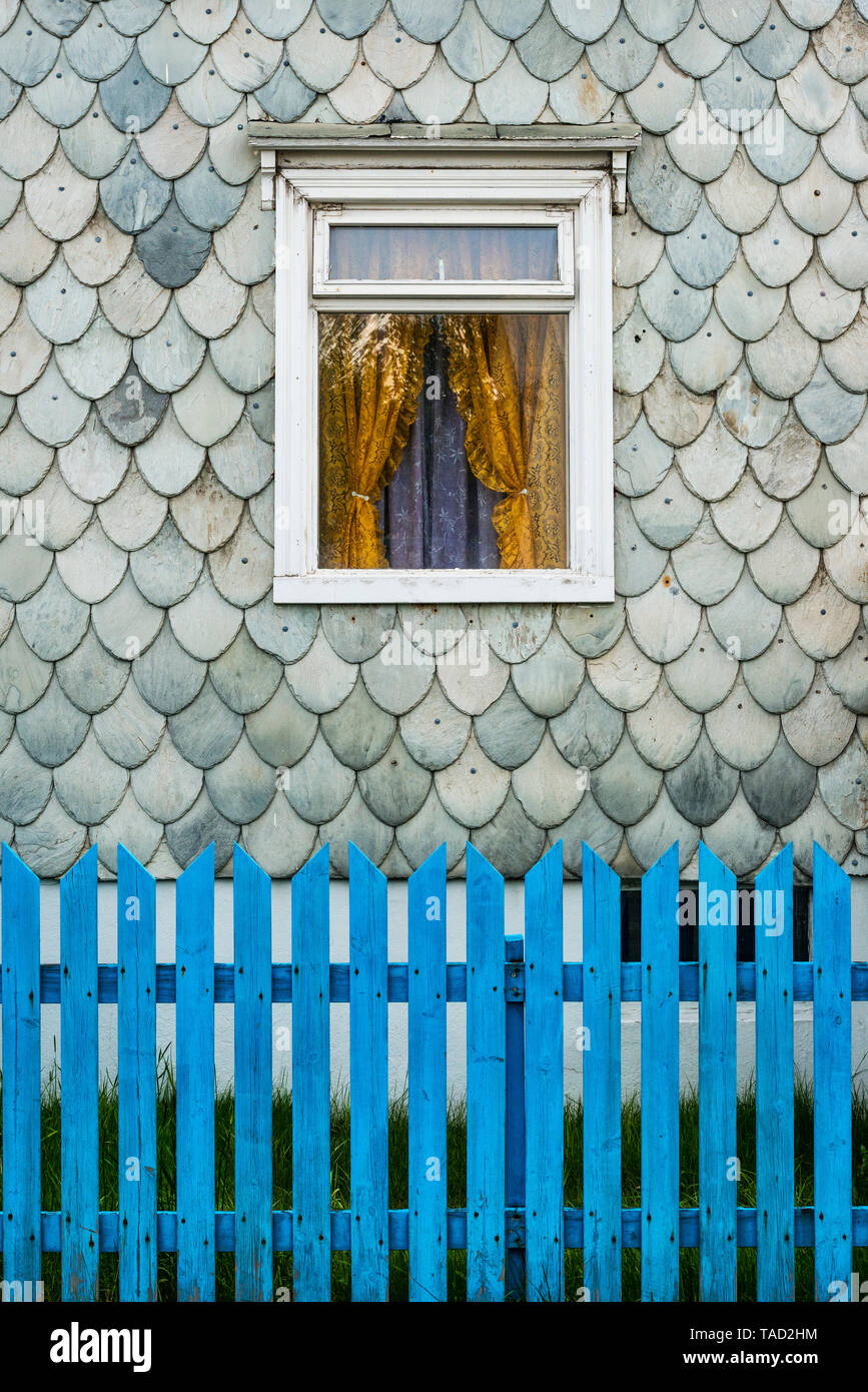 Akureyri, Islande du nord. Détail d'une vieille maison couverte de bardeaux d'ardoise arrondies dans un pattern des poissons, avec une clôture devant le jardin bleu Banque D'Images