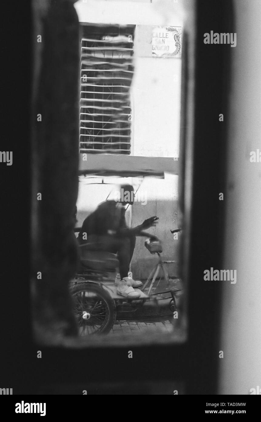 Cycle d'un conducteur de pousse-pousse, vu à travers une fenêtre tacheté, attend son prochain billet, La Havane, Cuba Banque D'Images
