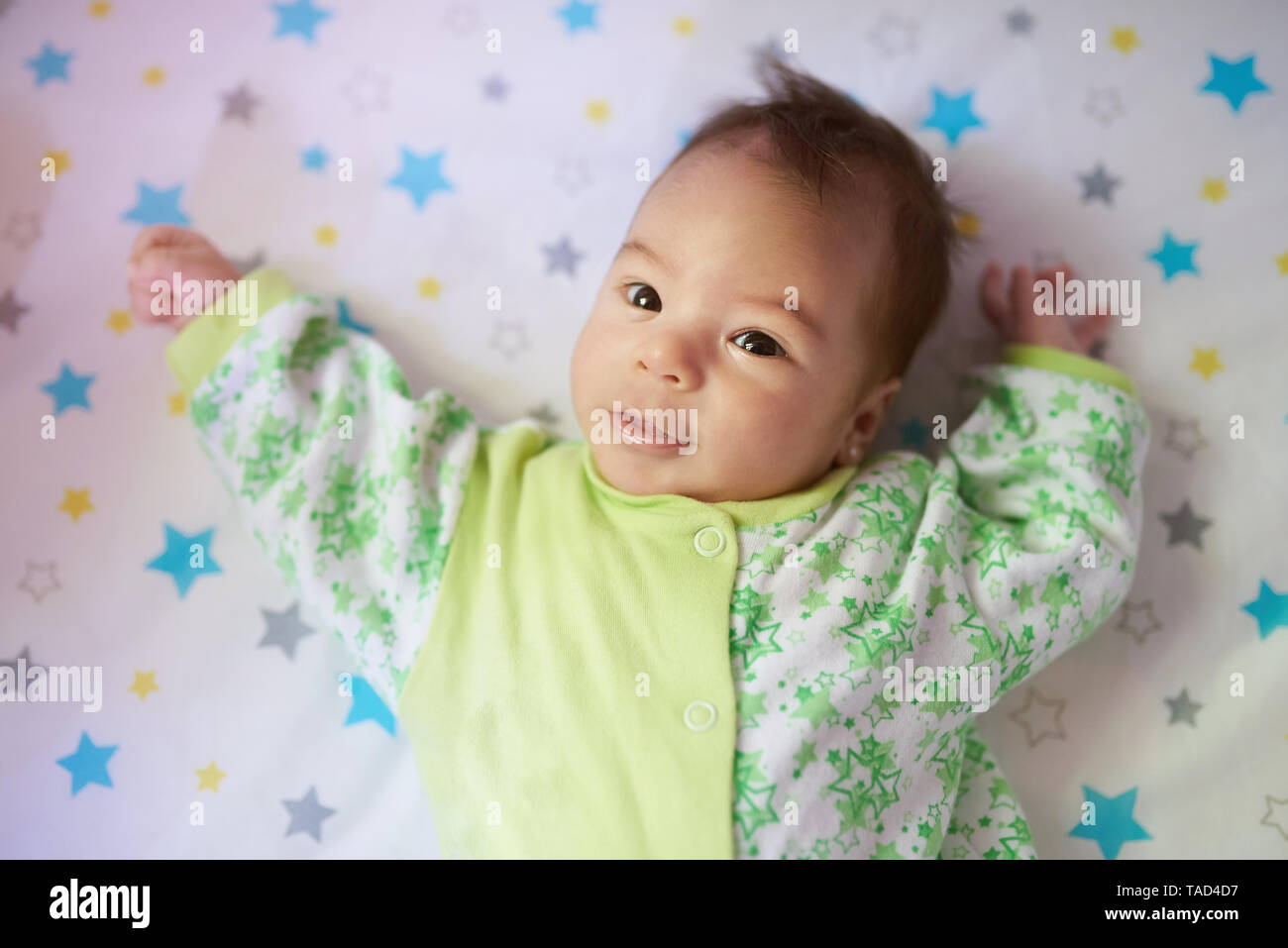 Close-up portrait of baby girl laying on bed in sunny day Banque D'Images