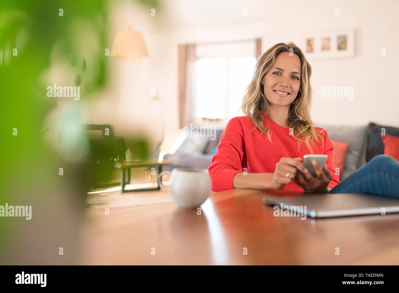 Portrait of smiling woman with laptop and cell phone sur table à manger à la maison Banque D'Images